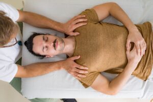 Massage therapist with white shirt holding his clients shoulders who is wearing a brown shirt during a massage session.