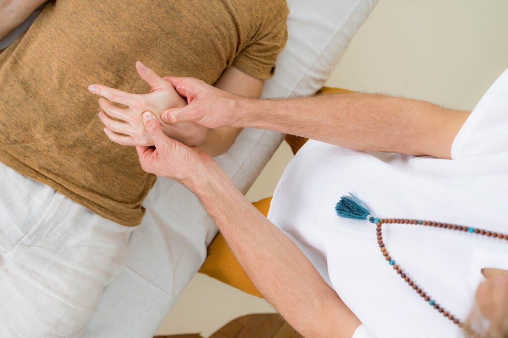 Massage therapist massages his clients hand with oil. Client is laying relaxed on the table, massage therapist sits upright.