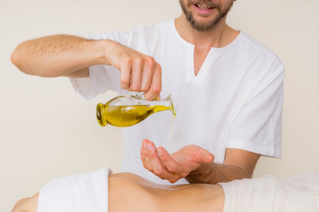 Massage therapist holds a bottle of massage oil that slowly pours into his hand.