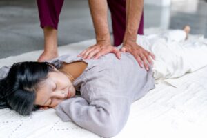 Woman laying on a massage mat wearing linen clothes while massage therapist massages her back.