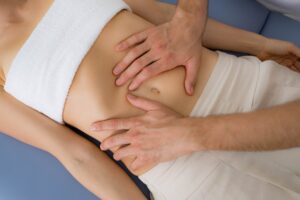 A person holding his hands on a womans belly, performing a abdominal massage.