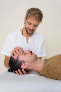 Massage therapist holding a clients head in a cupping manner performing a Cranio Sacral Therapy technique.