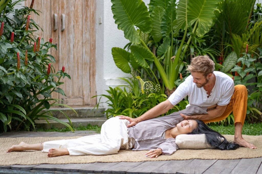 Massage therapist stretching a womans side body while performing a Thai massage in a green and lush environment.