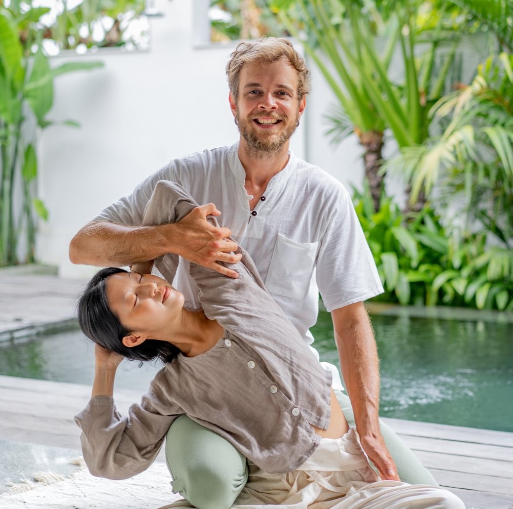 Massage therapist stretching a womans side body while performing a thai massage near a pool.