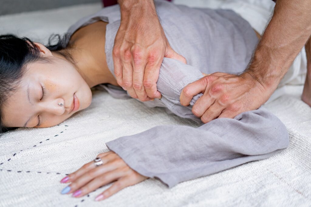 Man massaging a womans shoulder while she is face downwards laying on a linen cloth.