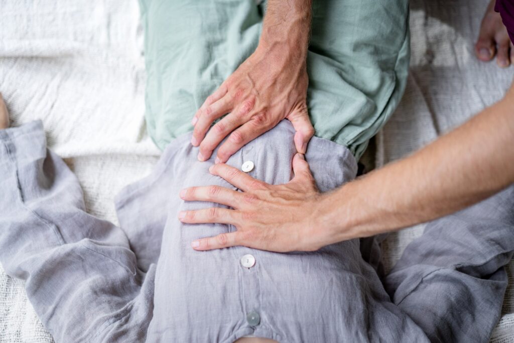 Man massaging a womans belly with both hands on linen clothes.