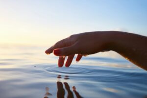 Hand floating above still sea water with water drops on the fingers, a few drops falling creating ripples.